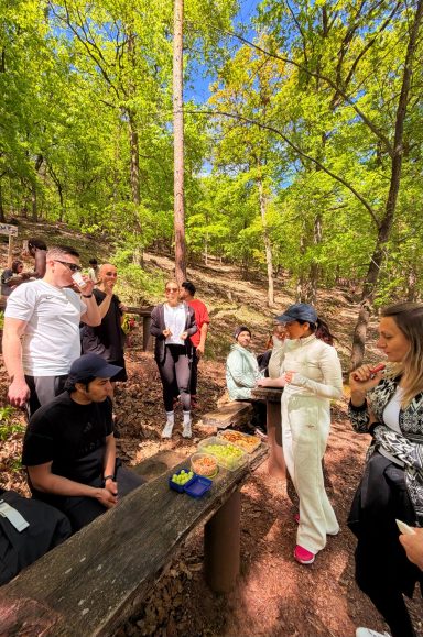 Gruppe von Menschen im Wald, die an einem Tisch essen und miteinander sprechen.