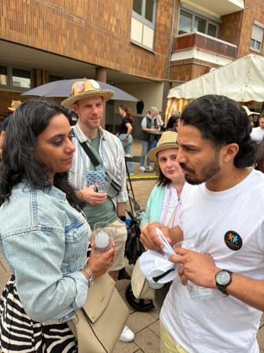 Drei Personen sprechen in einem urbanen Umfeld, während eine vierte im Hintergrund steht.